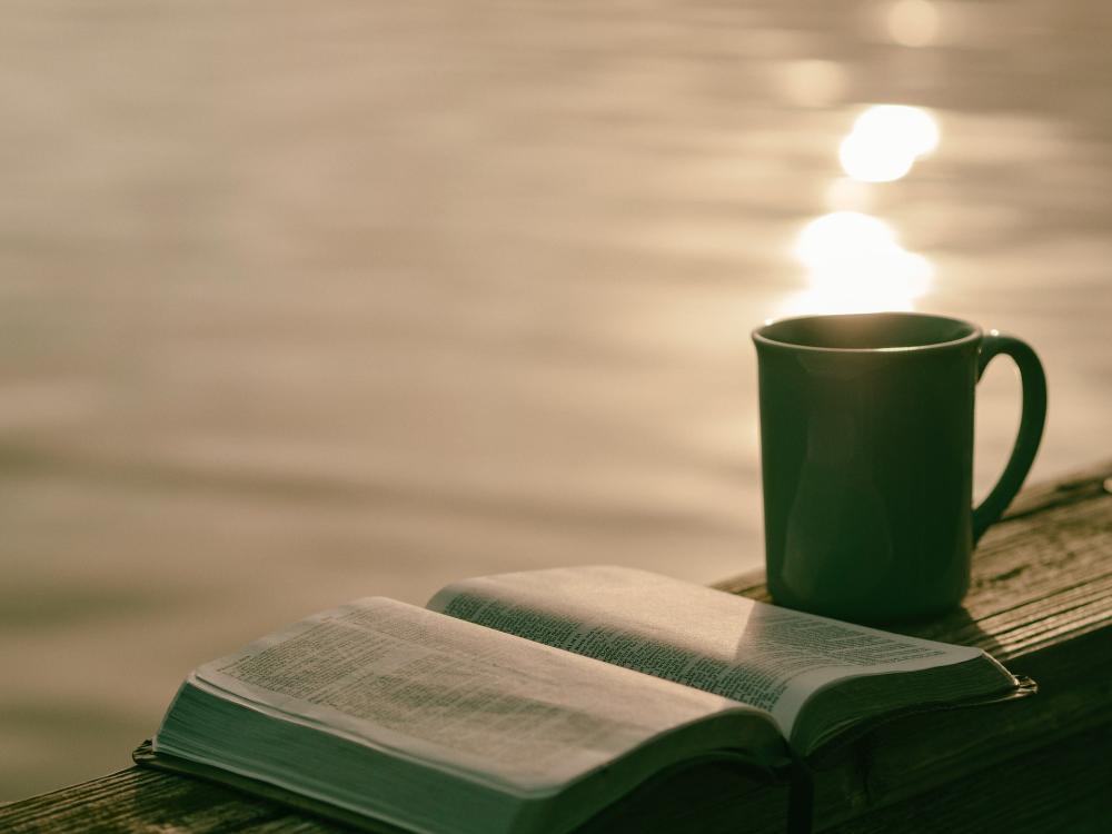 Raamattu on avattuna auringonnousun aikaan pöydälle, kuva Aaron Burden / Unsplash