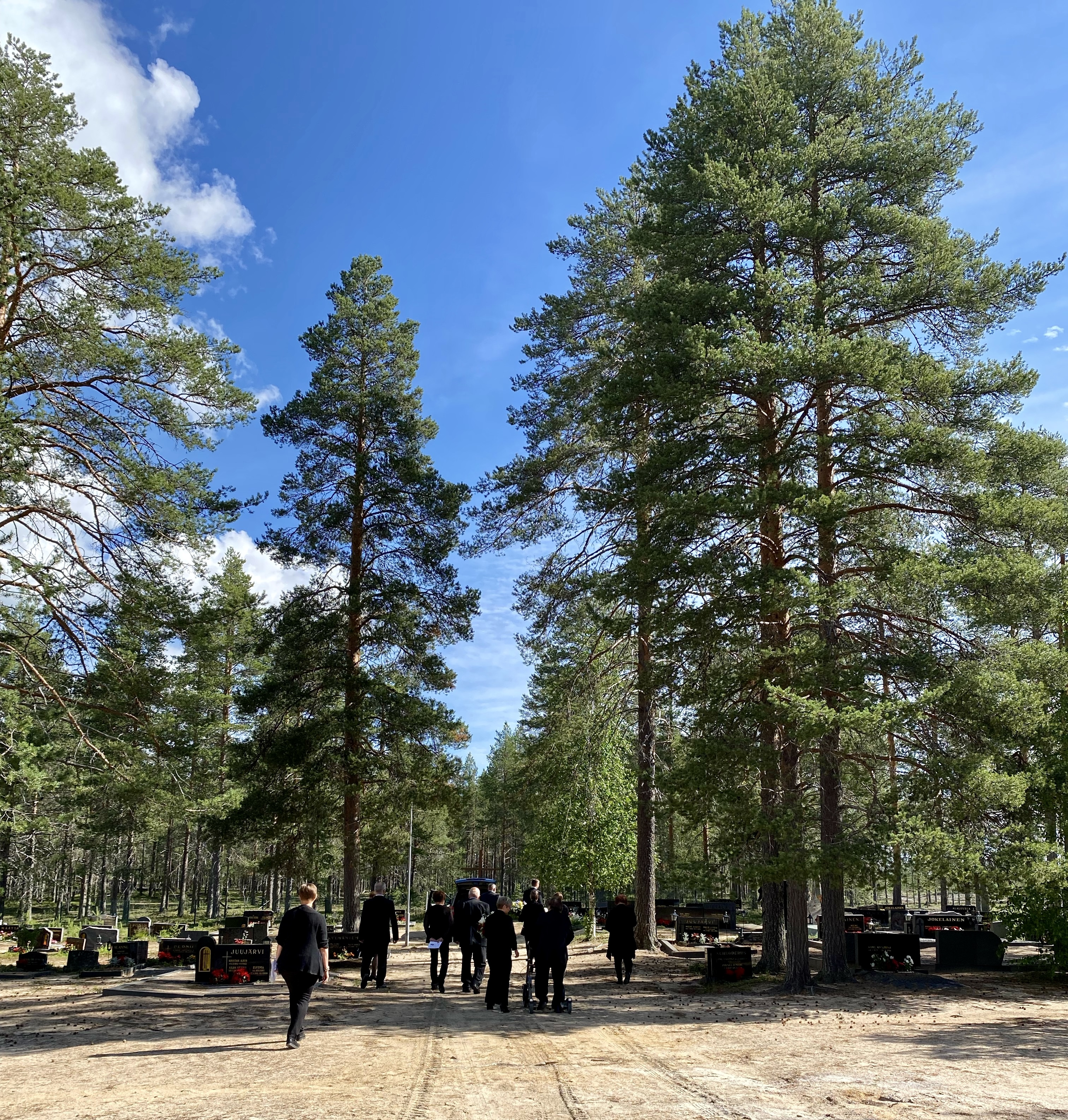 Kuva Juujärven hautausmaalta, joka on yksi pienimmistä, mutta yksi kauneimmista hautausmaista. Kuva otettu aurinkoisella säällä kesällä, kuvassa saattoväkeä. Kuva: Pentti Tepsa.